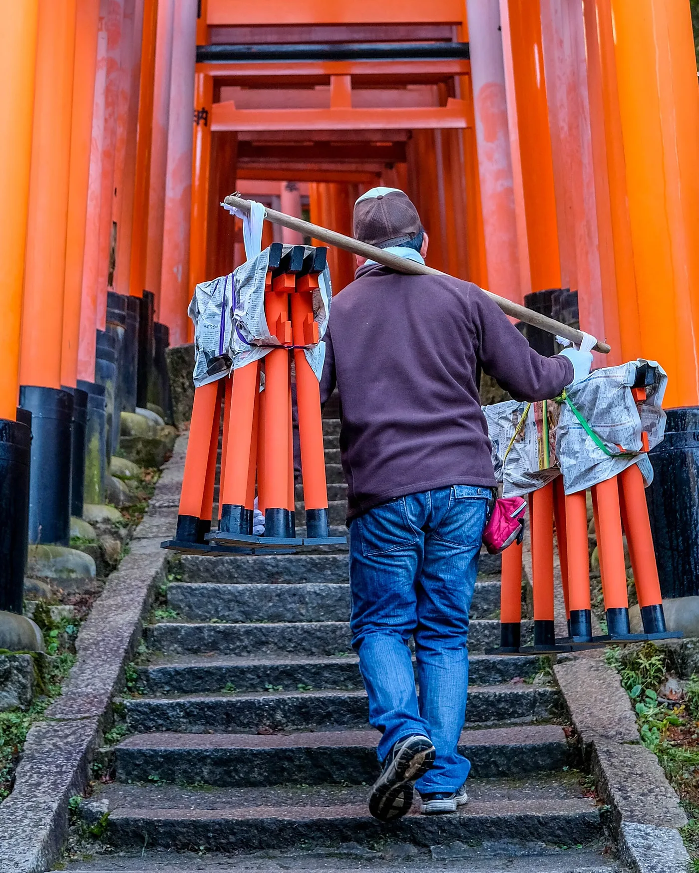 A worker carrying new torii uprights up the steps at Fushimi Inari